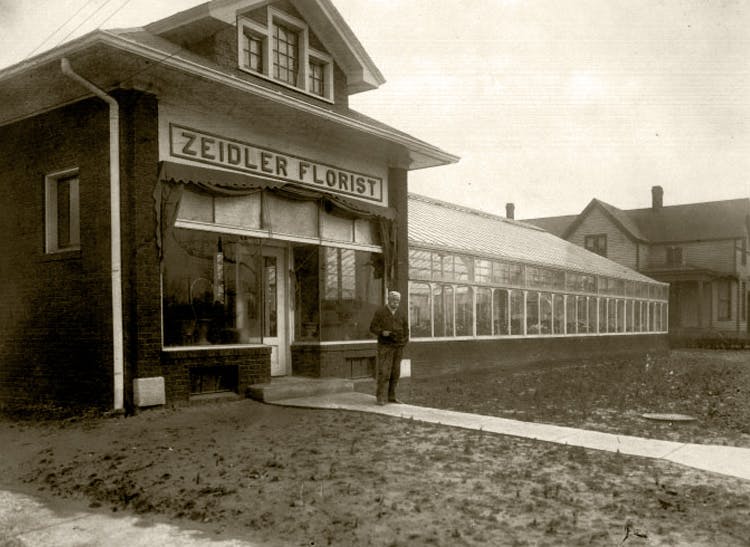 Karl Zeidler stands outside the floral shop and greenhouse that bears his name, circa 1900